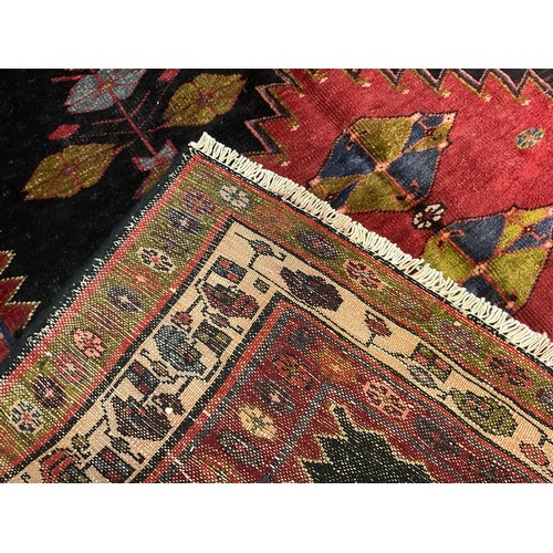 132 - A North west Persian Heriz rug / carpet, hand-knotted in dark tones of red, blue, and green, on a bl... 