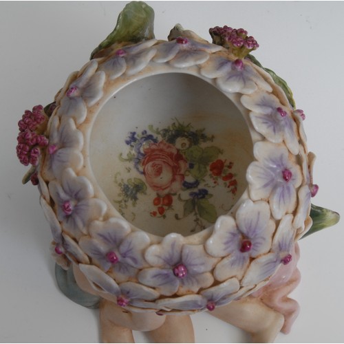 166 - A pair of Continental porcelain vases, each modelled with flowers supported by scantily clad putti, ... 