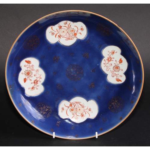 219 - A Chinese circular dish, painted in tones of iron red with flowers within shaped reserves on a blue ... 