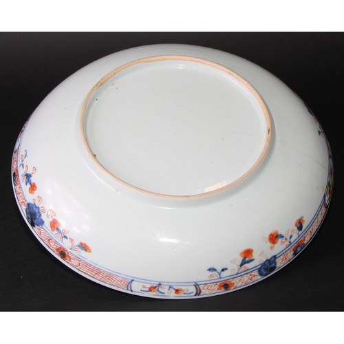 219 - A Chinese circular dish, painted in tones of iron red with flowers within shaped reserves on a blue ... 