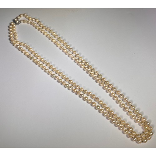 988 - A two string pearl necklace, the silver clasp set with two pearls, approximately 80cm total length