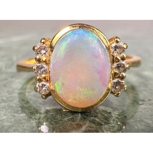 1027 - An opal and diamond ring, central oval cabochon opal flashing vibrant blue green play, between three... 