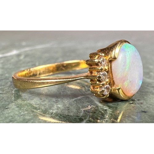 1027 - An opal and diamond ring, central oval cabochon opal flashing vibrant blue green play, between three... 