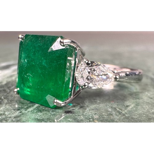 1025 - An Emerald and diamond ring, central square emerald cut emerald, approx 6.05ct mounted between pear ... 