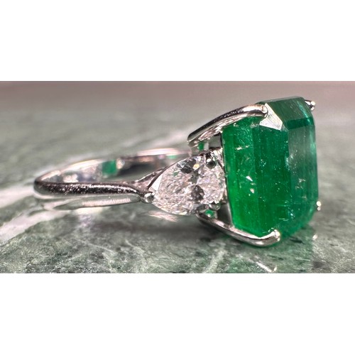 1025 - An Emerald and diamond ring, central square emerald cut emerald, approx 6.05ct mounted between pear ... 