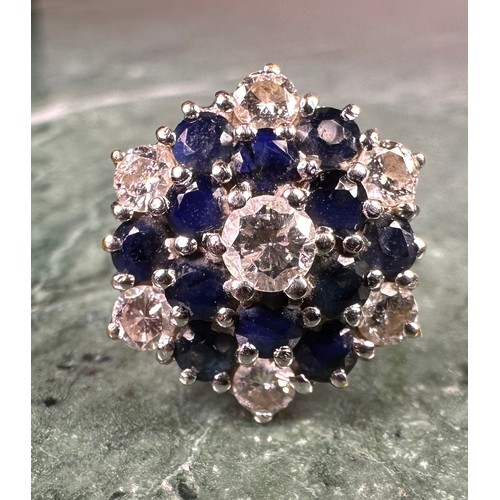 1006 - An 18ct gold diamond and sapphire flowerhead cluster ring, the central brilliant cut diamond flanked... 