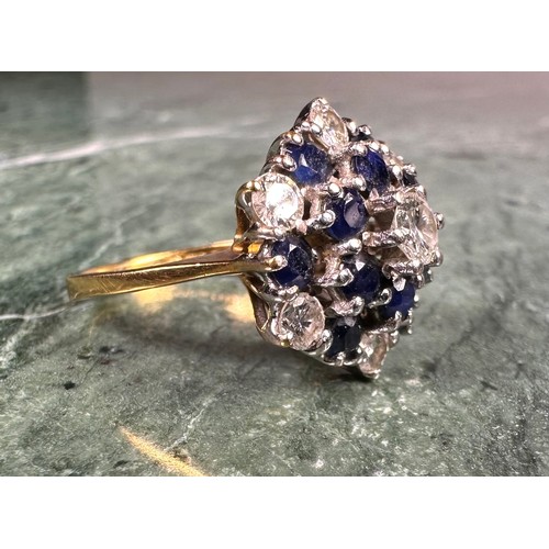 1006 - An 18ct gold diamond and sapphire flowerhead cluster ring, the central brilliant cut diamond flanked... 