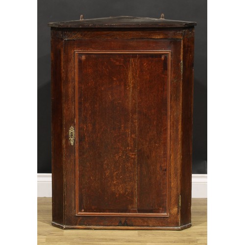 2087 - An 18th century oak wall-hanging corner cupboard, of unusual proportions, applied shaped cut-card fr... 