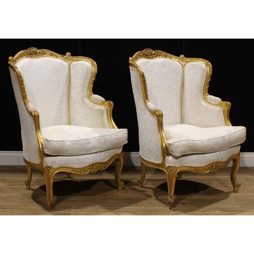 1601 - A pair of Louis XV Revival giltwood bergère cabriolet, stuffed-over upholstery, squab cushion, 101.5... 