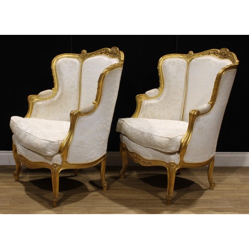 1601 - A pair of Louis XV Revival giltwood bergère cabriolet, stuffed-over upholstery, squab cushion, 101.5... 