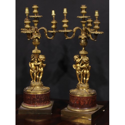 2162 - A pair of French gilt bronze figural five light candelabra, the pillars cast with putti, marble socl... 