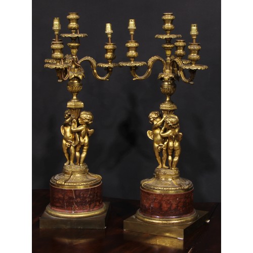 2162 - A pair of French gilt bronze figural five light candelabra, the pillars cast with putti, marble socl... 