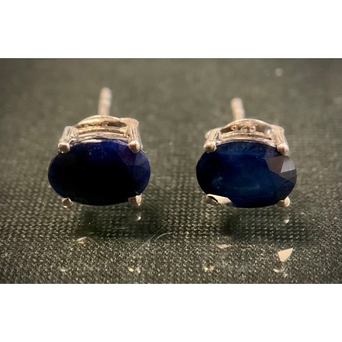 473 - A pair of oval deep blue treated sapphire stud earrings, silver mounts, 1.7g gross