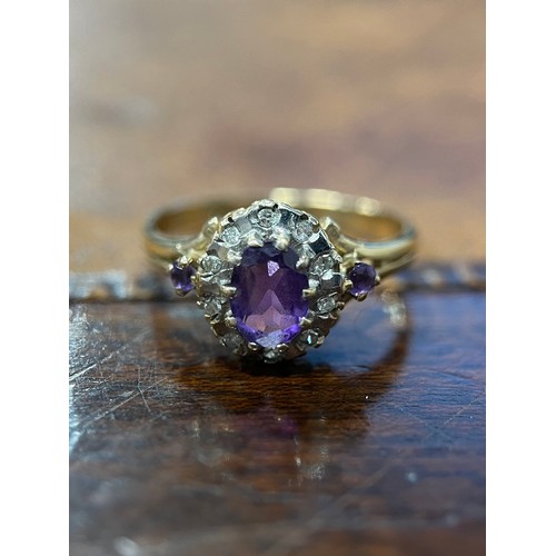 653 - A 9ct gold, amethyst and diamond cluster ring, the central oval facet cut stone within a band of rou... 