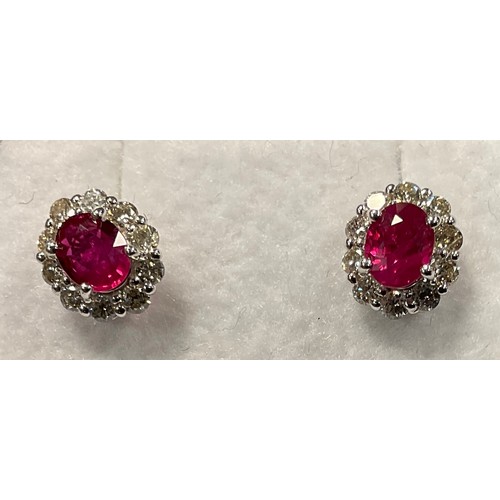 438 - A pair of ruby and diamond oval cluster earrings, central red ruby surrounded by a halo of brilliant... 