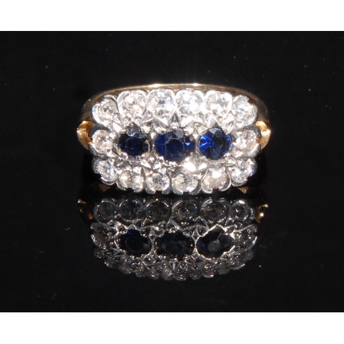 685 - A diamond and sapphire cluster ring, rounded rectangular crest set with three blue sapphires surroun... 