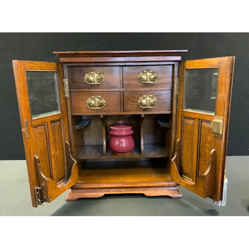 42 - An Edwardian oak smokers cabinet, two door front enclosing fitted interior with four drawers above t... 