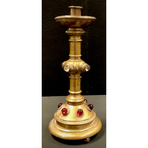 52 - An Arts and Crafts brass altar candlestick, inset with ruby coloured and clear glass cabochons, on c... 