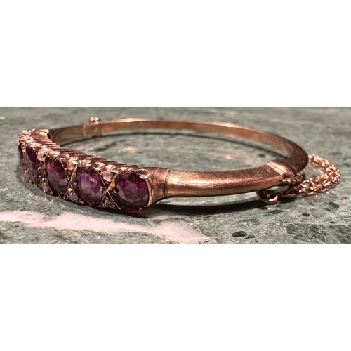 857 - A ruby and diamond hinged bangle, the seven graduated oval facet cut stones divided by pairs of diam... 