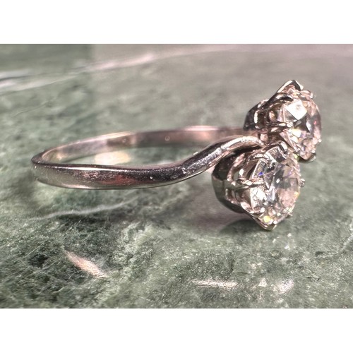 877 - A two-stone diamond cross-over ring, the two round brilliant cut stones claw set, each approximately... 