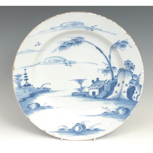 104 - An 18th century Delft circular dish, painted in the Chinese taste with a pagoda in a landscape, 31cm... 