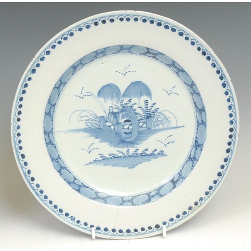 105 - An 18th century Delft circular dish, painted in tones of blue in the Chinese taste with a flowering ... 