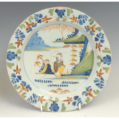 107 - An 18th century Delft circular plate, painted in the Chinese taste with a lady in a garden, 21.5cm d... 