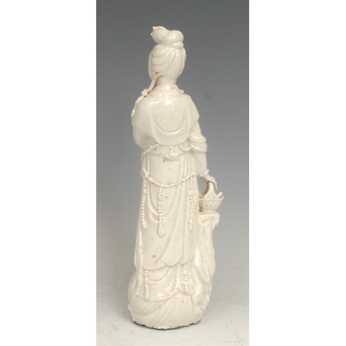 385 - A Chinese blanc de chine figure, Guanyin, she stands, holding a basket, 26cm high, 18th century