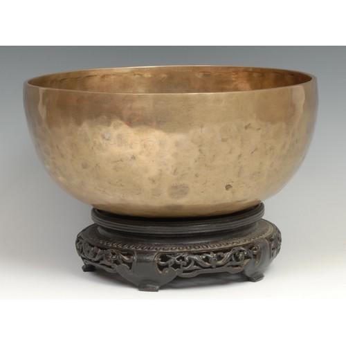 377 - A Tibetan bronze singing bowl, feint inlaid inscription, 27cm diam, pierced and carved hardwood stan... 