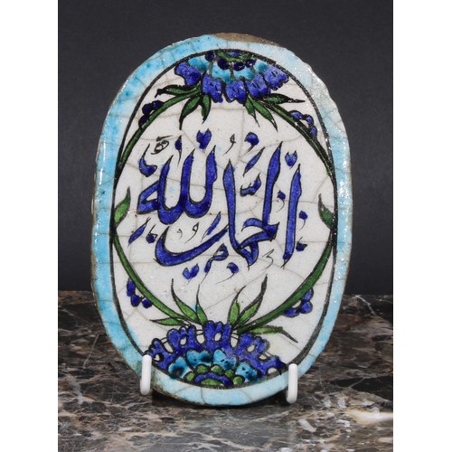 350 - A Middle Eastern oval tile, painted in the Iznik palette with stylised flowers and inscribed with Ar... 