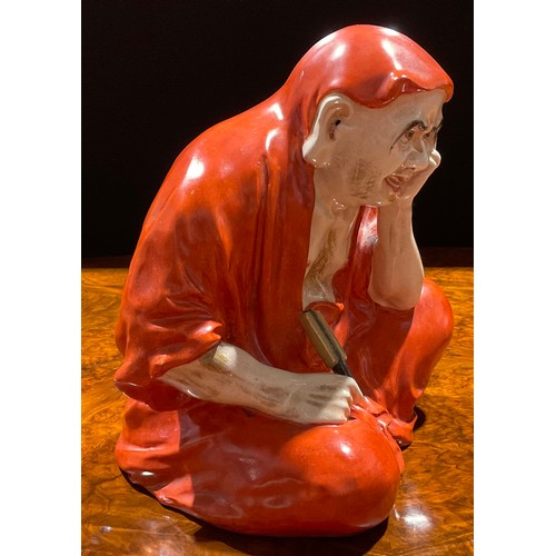 463 - A Japanese porcelain figure, as a Daruma Monk, seated holding a fan, wearing loosely fitting robes, ... 