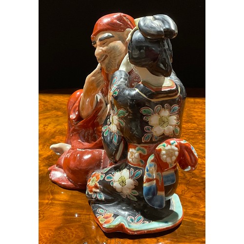 462 - A Japanese porcelain figure group, as a seated robed monk with Geisha attendant cleansing his ear, p... 