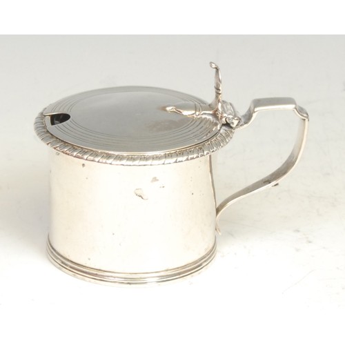 600 - A George IV silver drum mustard, hinged cover, gadrooned border, angular scroll handle, blue glass l... 