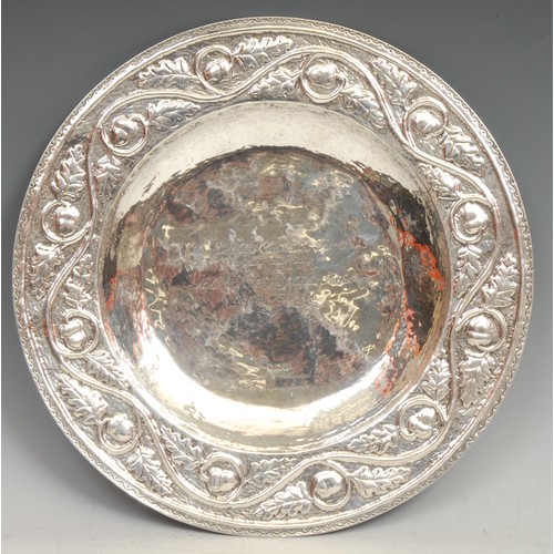 753 - An Arts and Crafts silver circular charger, planished overall and chased with a border of fruiting o... 