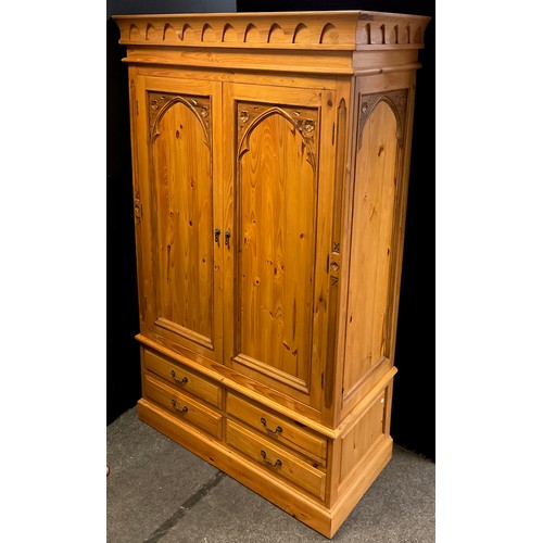 102 - A Gothic style pine double wardrobe, having a pair of doors with Gothic arch carved panels, above fo... 