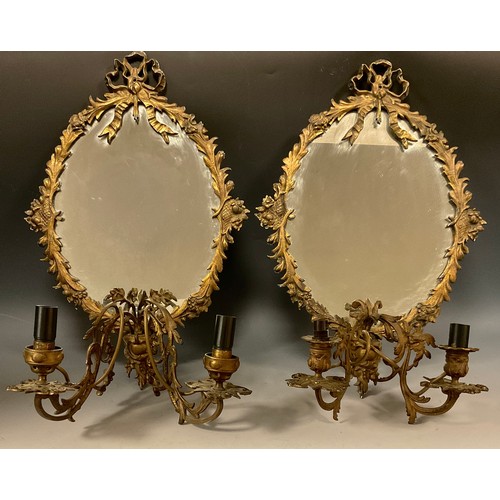 1653 - A near pair of Louis XVI Revival brass girandoles, each with an oval mirror plate and ribbon-tied le... 