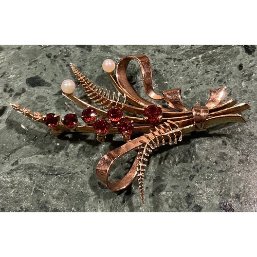 943 - A 9ct gold garnet and seed pearl brooch, cast as a spray of ribbon tied ferns and budding stems, the... 