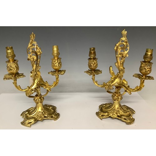 3279 - A pair of ornate cast iron two branch candelabras, gilt, the crest a scrolling acanthus, terminating... 