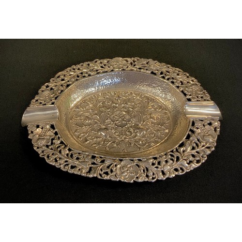 321 - An Indonesian silver coloured metal oval dish, intricately embossed with floral motifs within simila... 