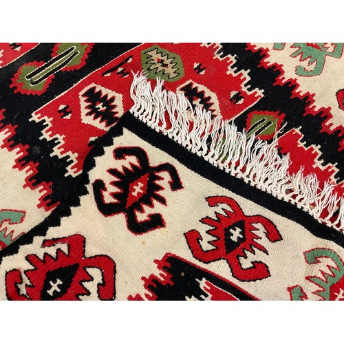 33 - A Turkish Kilim rug, hand-knotted with abstract motifs, in tones of red, black, blue, green, and cre... 