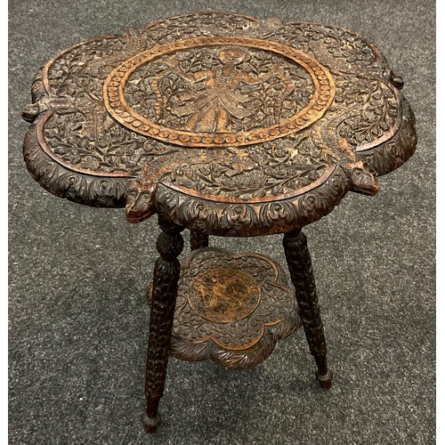 66 - An Indian carved occasional table, intricately decorated with a figure of a snake charmer, lizards a... 