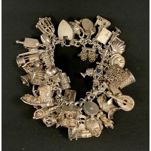 334 - A large silver charm bracelet suspending over forty charms inc Miners Lamp, Moon with American fold ... 