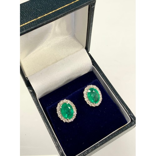 370 - A pair of emerald and diamond cluster earrings, each with a central oval emerald surrounded by eight... 