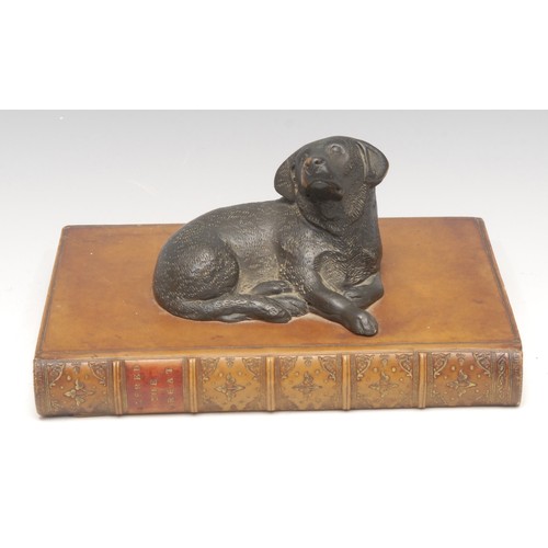 3293 - Interior Decoration - a cold cast desk model, of a dog, recumbent upon a leather bound book, 18.5cm ... 