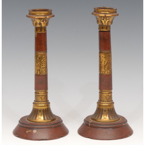 3155 - A pair of Egyptian Revival red marble and lacquered brass columnar candlesticks, 18cm high, c. 1870