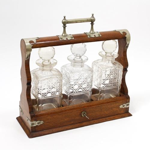 3137 - A late Victorian oak three-bottle tantalus, the E.P.N.S cut-card mounts in the Gothic taste, canted ... 