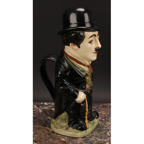 27 - A Royal Doulton jug and cover, modelled as Charlie Chaplin, he stands wearing baggy black suit with ... 