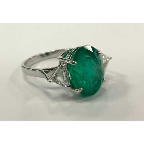 335 - An emerald and diamond ring, central oval emerald approx 5.63ct, between trilliant cut diamond shoul... 