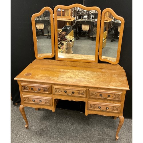 121 - A French Provincial style oak dressing table, serpentine shaped triple mirror, above a base with fiv... 