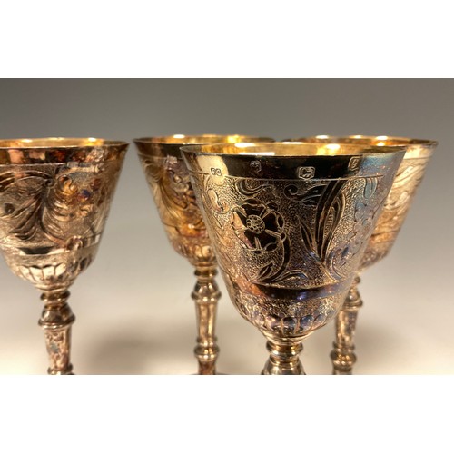 70 - A set of four Elizabeth II silver wine goblets, each with gilt bowls, embossed floral and foliate co... 